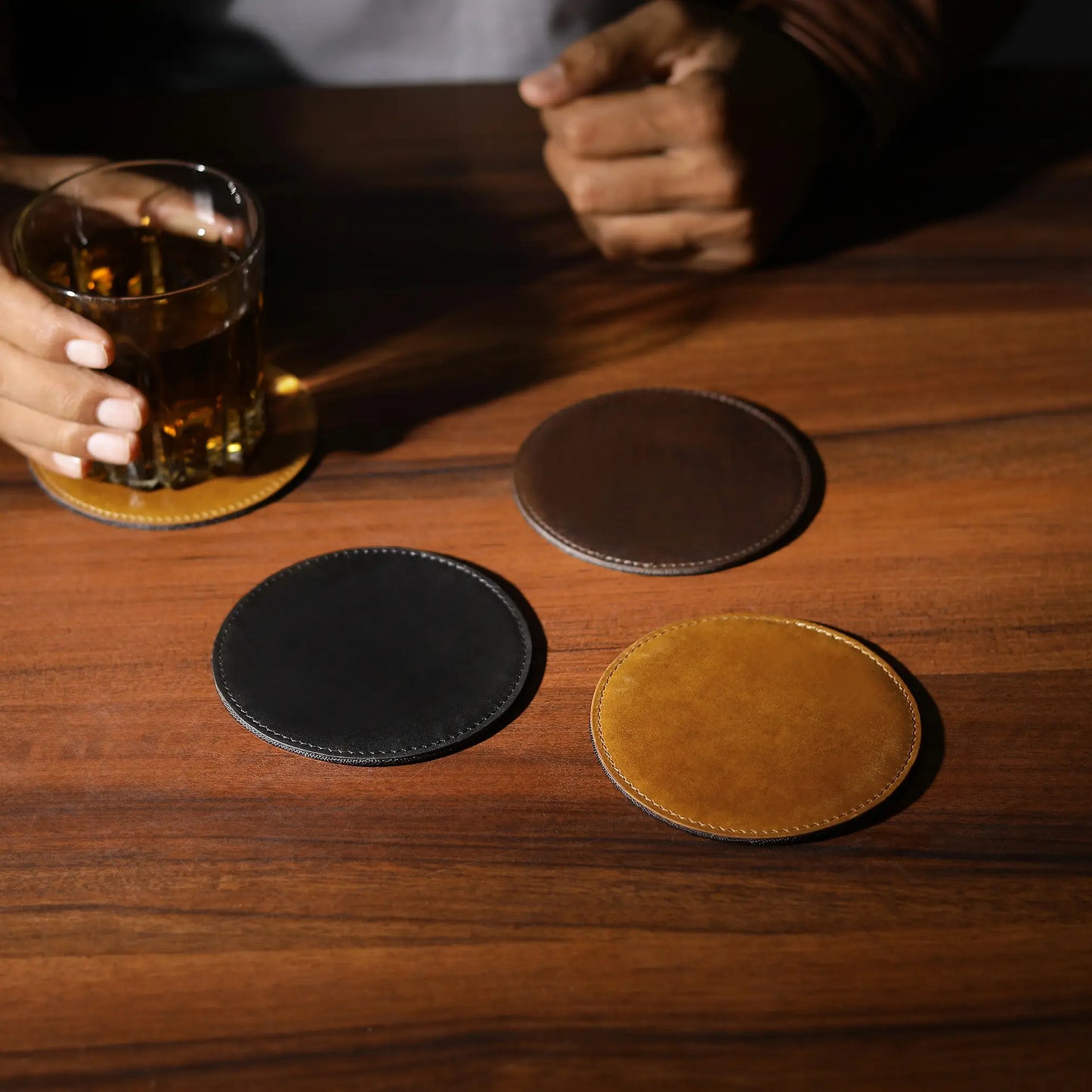 Three leather coasters on a wooden table with a glass of beer.