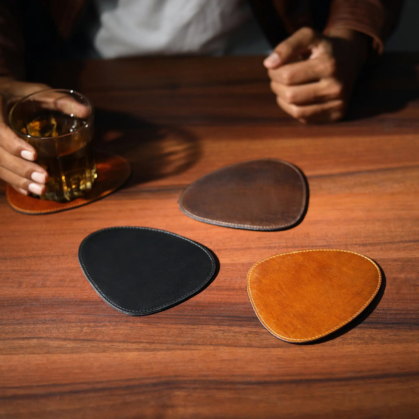 Three leather coasters on a wooden table with a glass of whiskey.