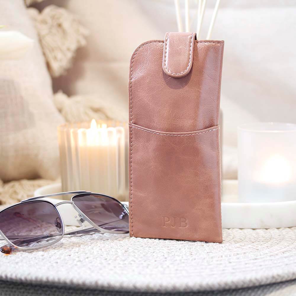 Pink leather pouch with sunglasses on a textured surface with soft lighting