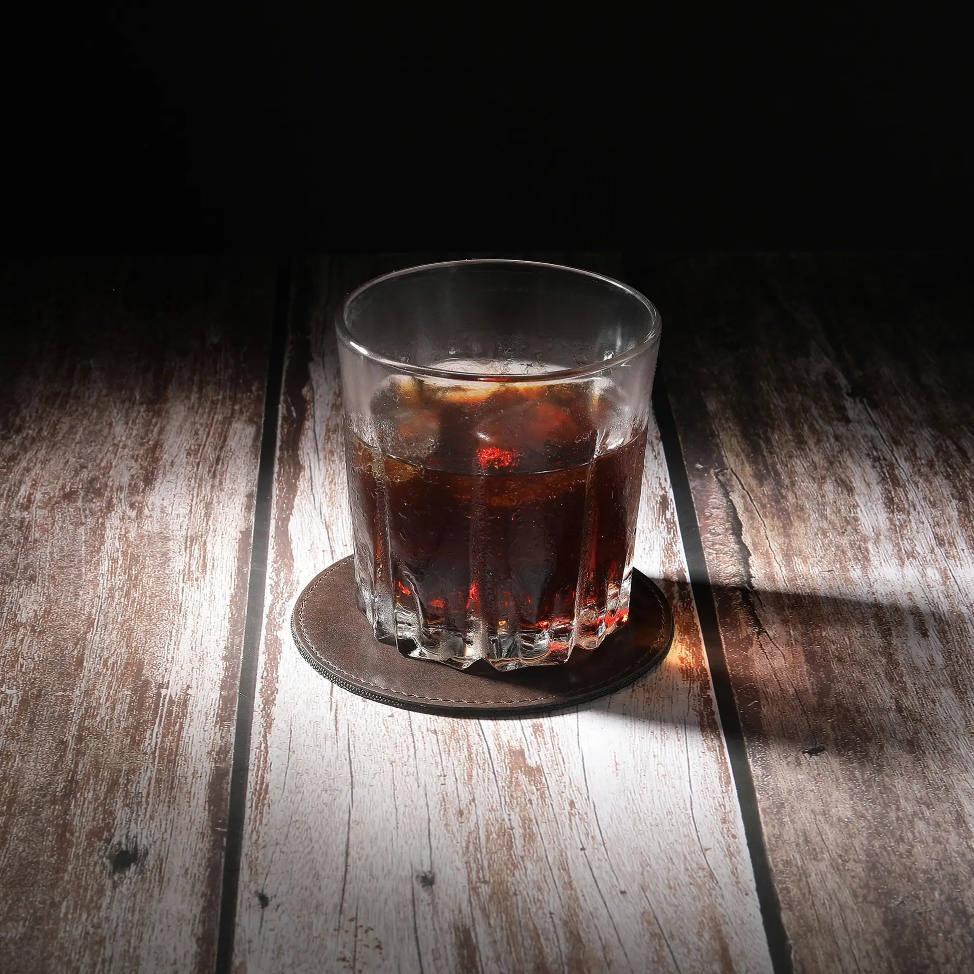 Glass of dark liquid on a brown leather coaster  with a dark background