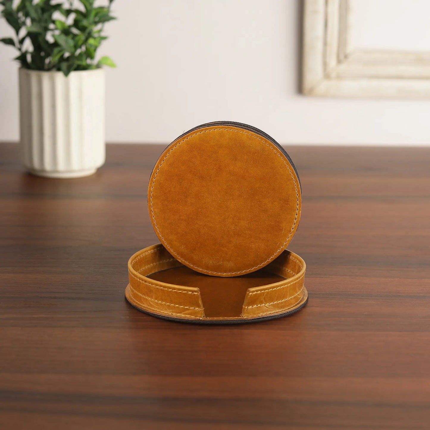 Set of round tan leather coasters on a wooden surface with a plant in the background.