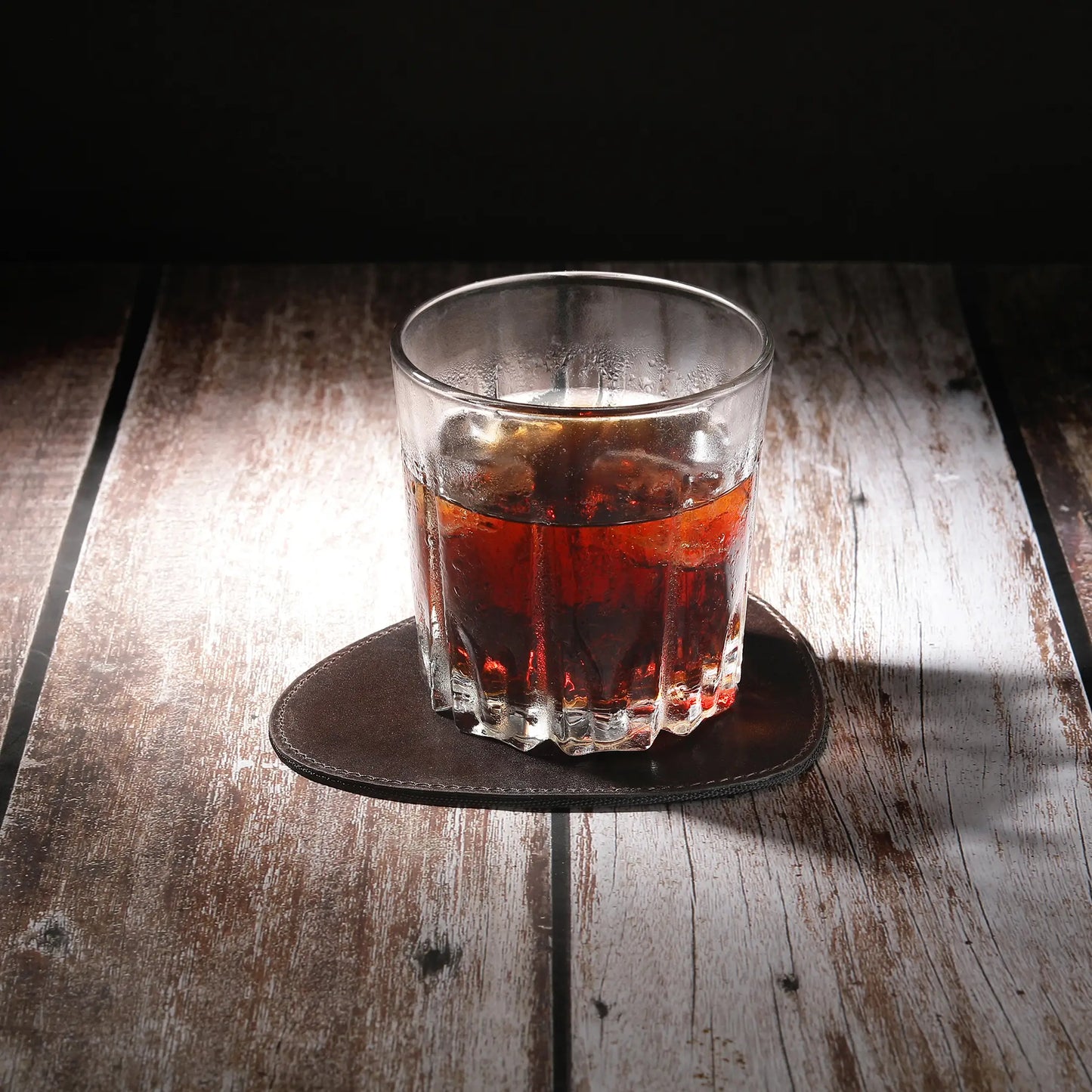 Glass of red liquid on a brown leather coaster  surface with a dark background