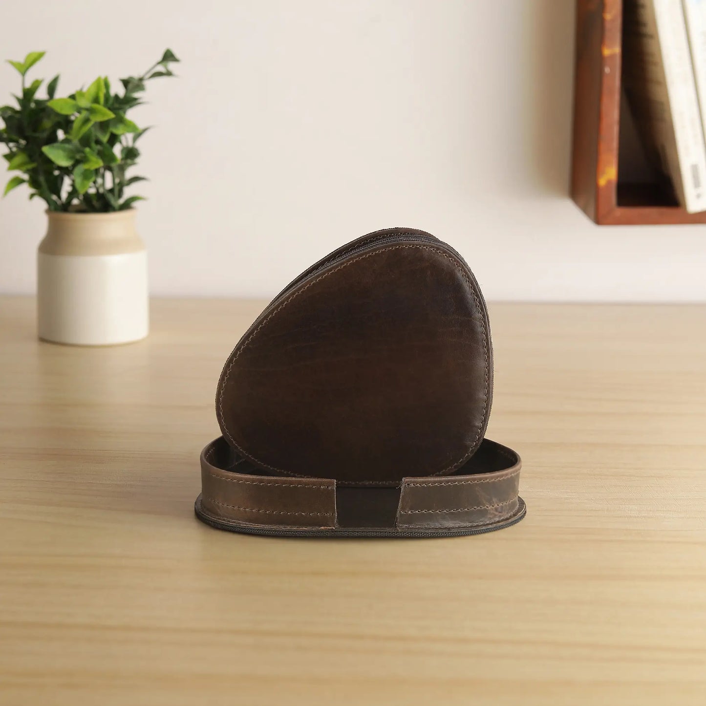 Brown leather coasters on a wooden surface with a plant and books in the background