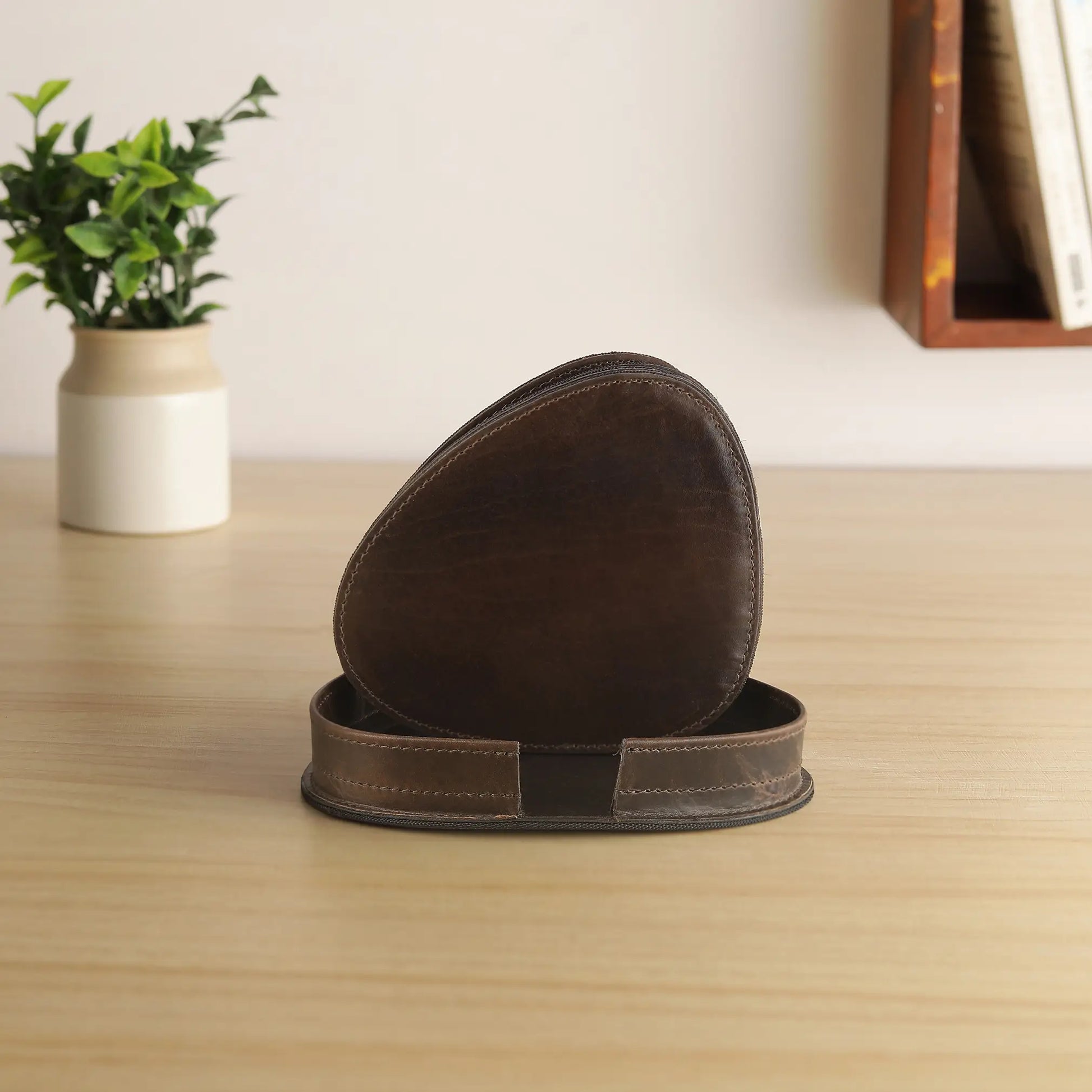 Brown leather coasters on a wooden surface with a plant and books in the background