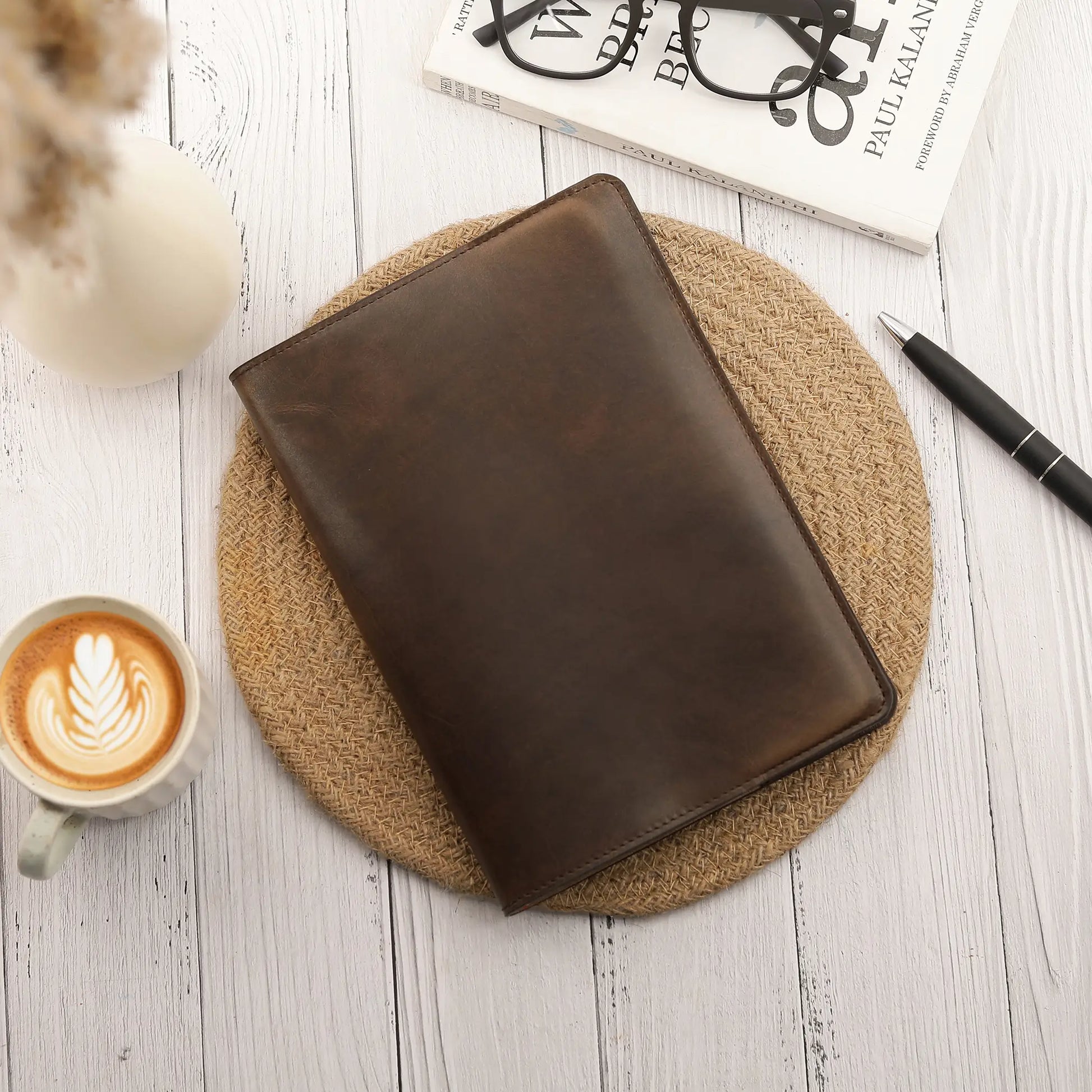 Brown leather diary cover on a woven coaster with a cup of coffee and pen on a wooden surface