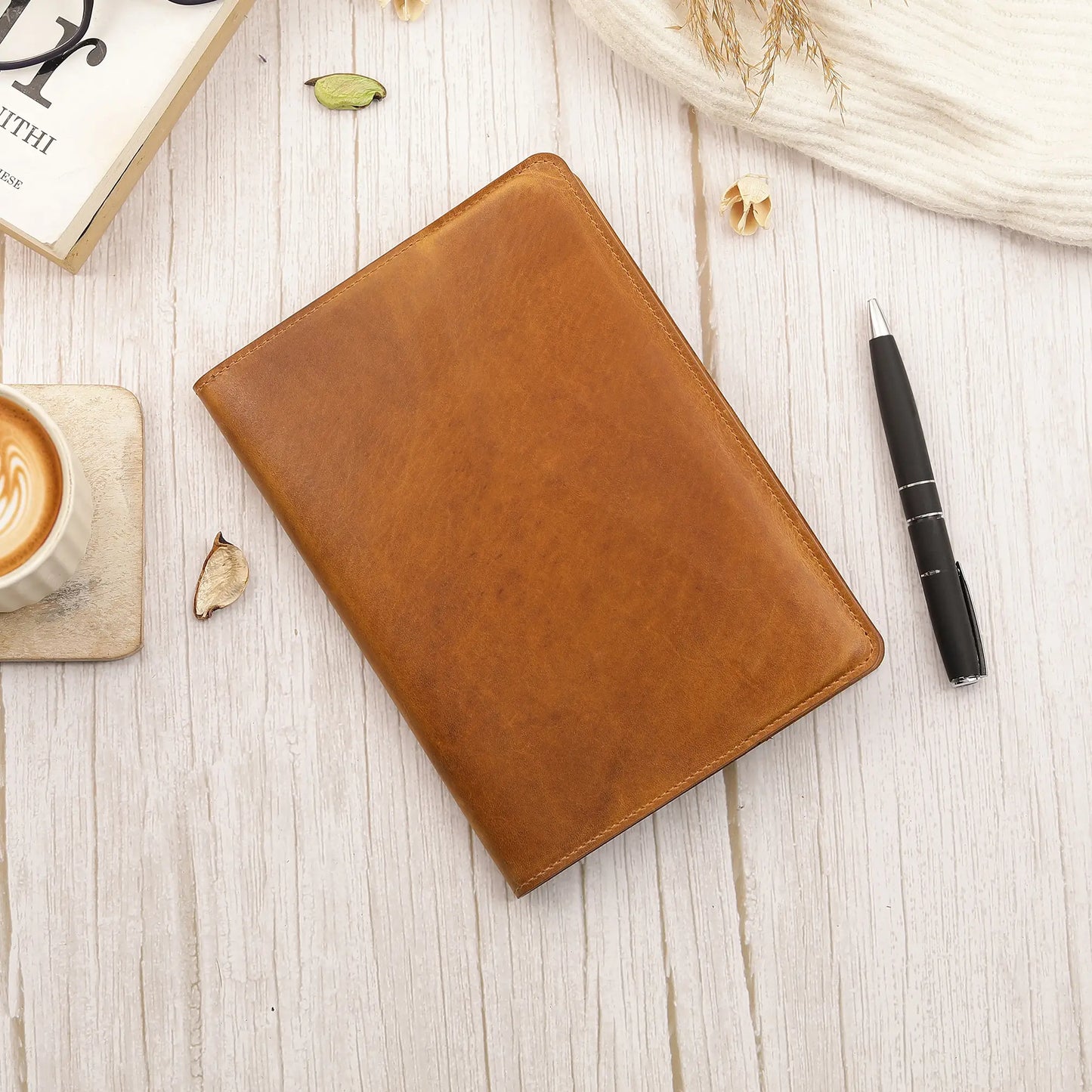 Tan leather diary cover on a light wooden surface with a pen and coffee cup.