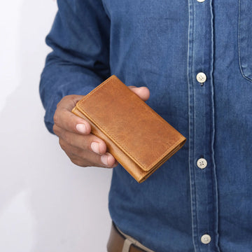 Person holding a tan leather wallet against a white background