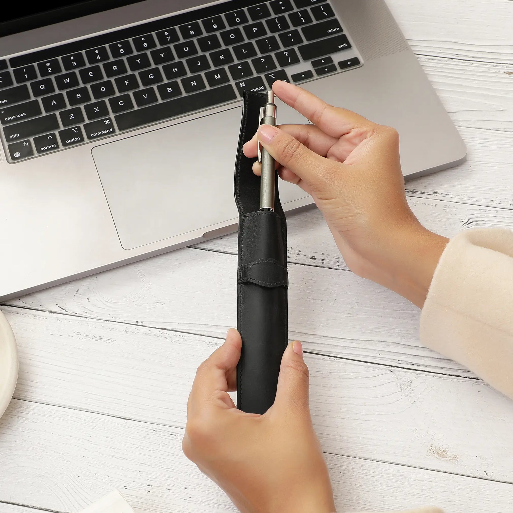 Person using a black leather  pen holder with a laptop on a white wooden surface