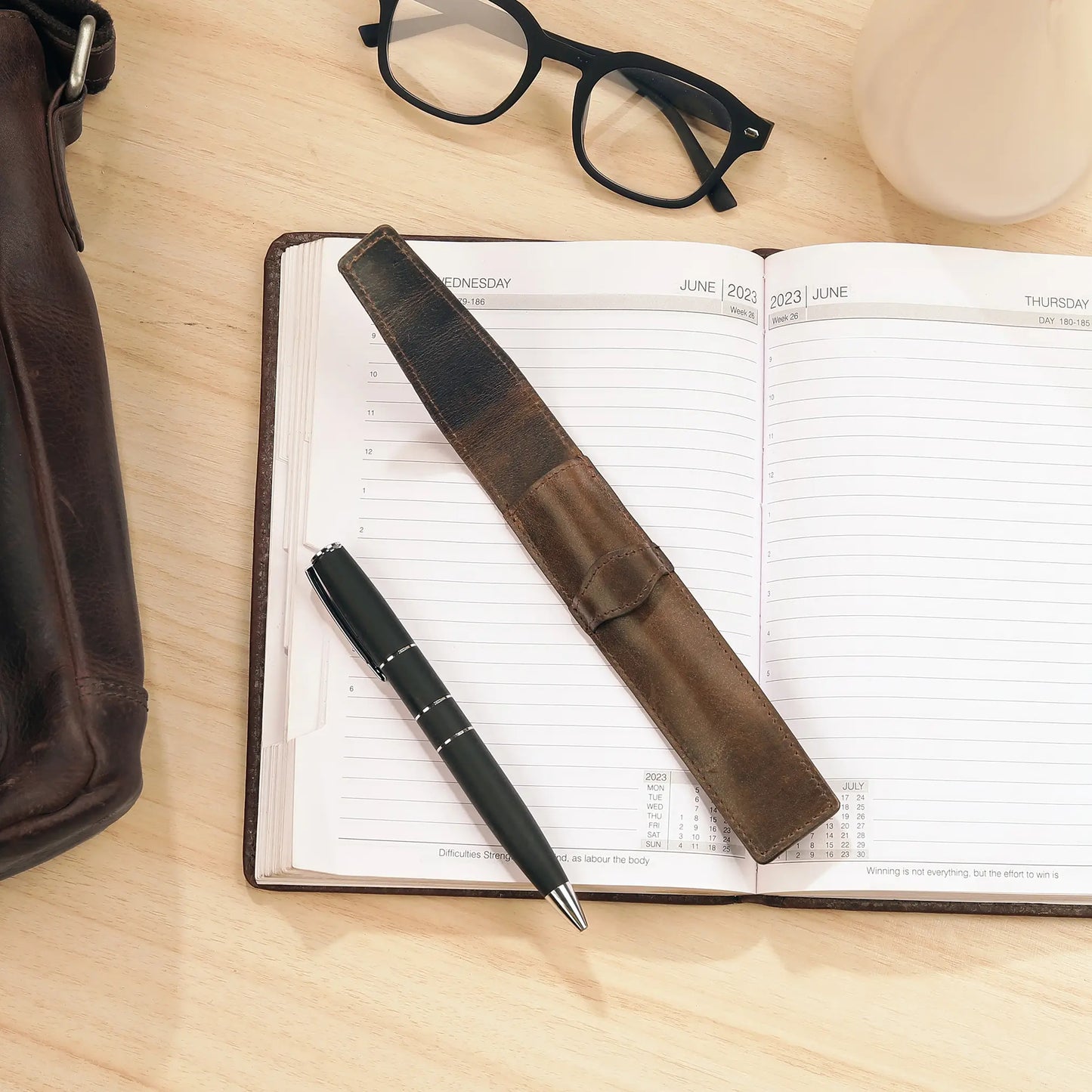 Open planner with leather pen holder and pen on a wooden surface