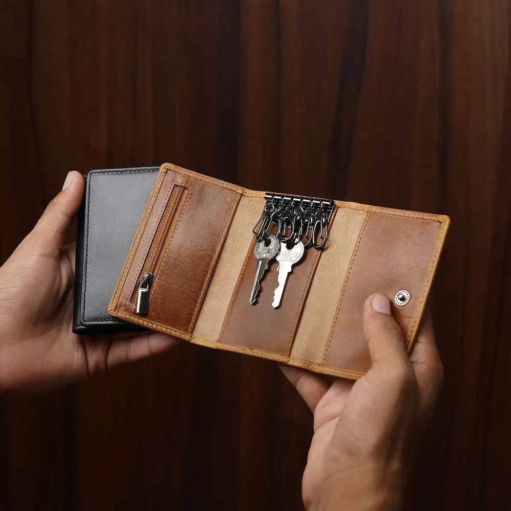 Tan leather wallet with keys held by hands against a dark background